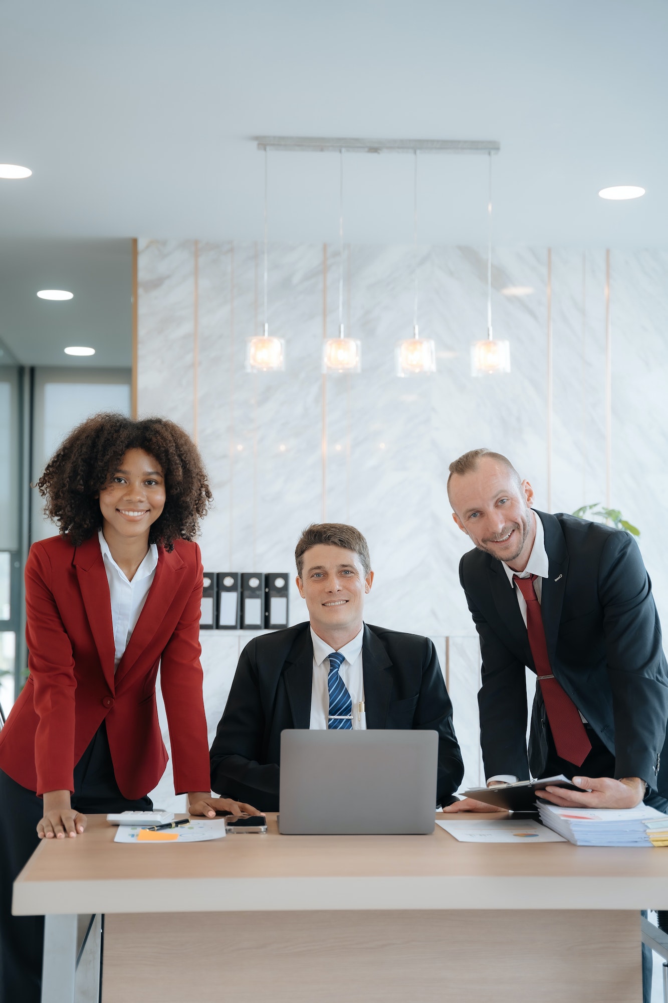 Business team smiling and confident standing in front of bright desk.